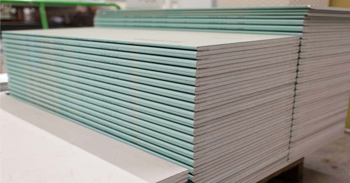 Drie stapels gyprocplaten op een palet in een magazijn. De voorste stapel bevat witte platen en is erg laag, de middelste stapel bevat groene gyprocplaten en is erg hoog, de achterste stapel bevat ook groene gyprocplaten en is nog hoger dan de middelste.