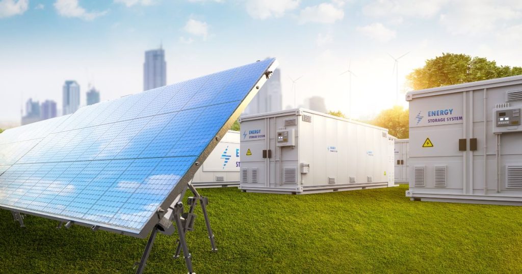 Een groot industrieel zonnepaneel op een grasveld, met daarachter verschillende grote industriële batterijen.