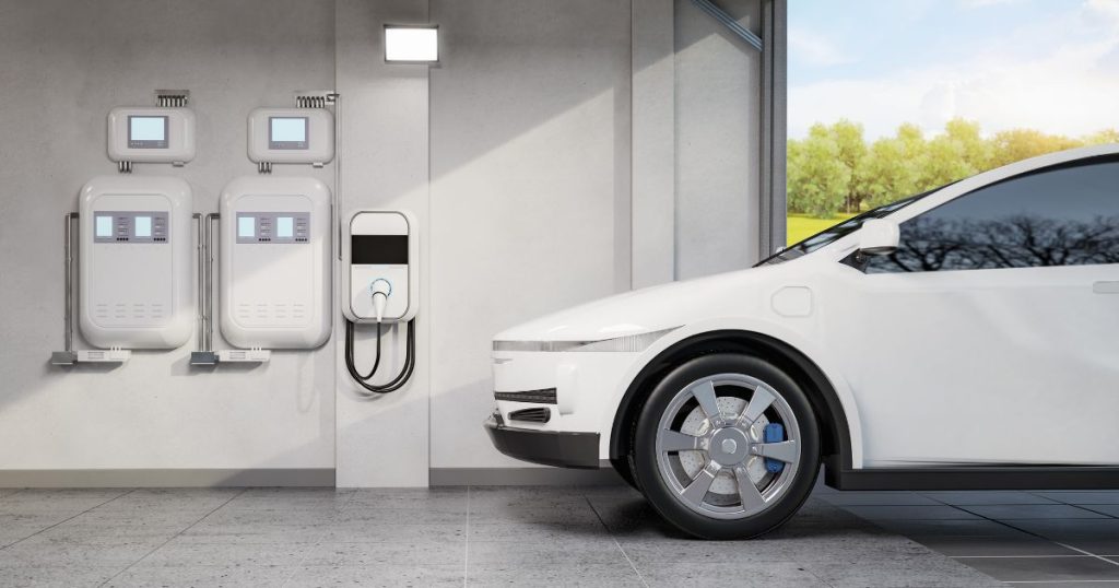 Een garage met witte wanden, een witte elektrische auto, twee grote thuisbatterijen, twee omvormers en een laadpaal in wandmodel.