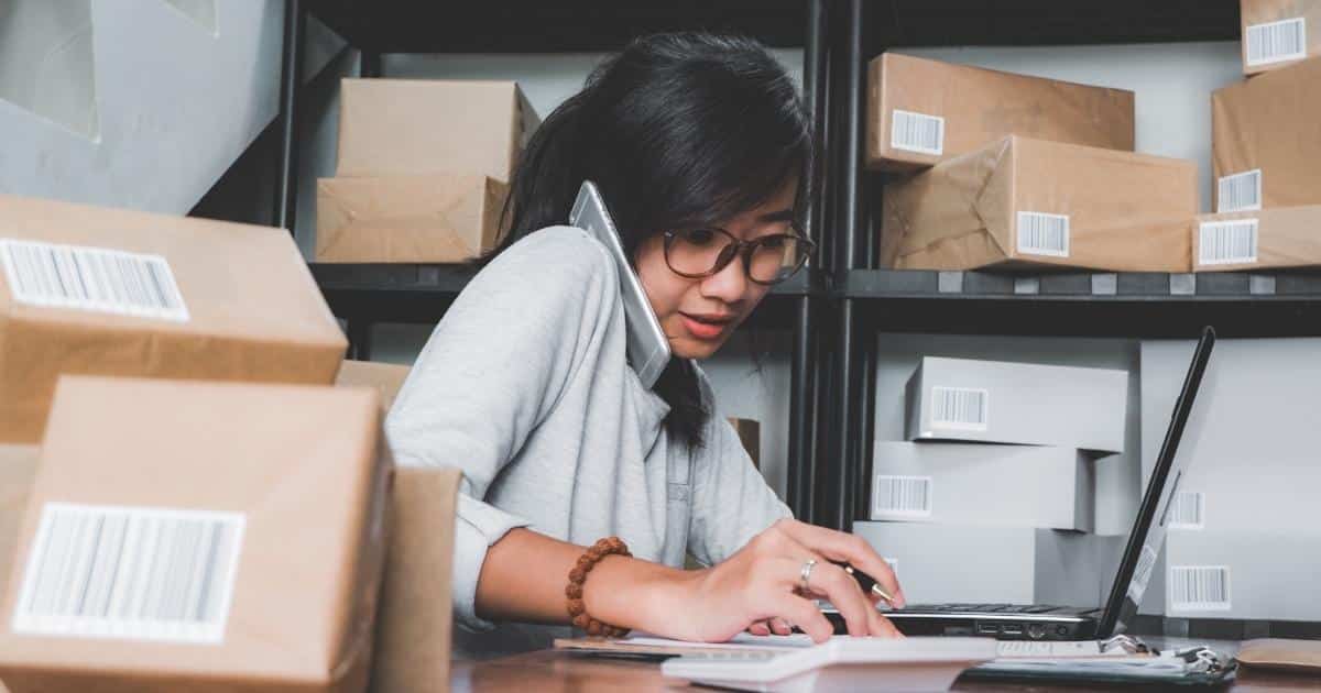 Student aan het werk in een bedrijf terwijl ze belt en op een laptop werkt.
