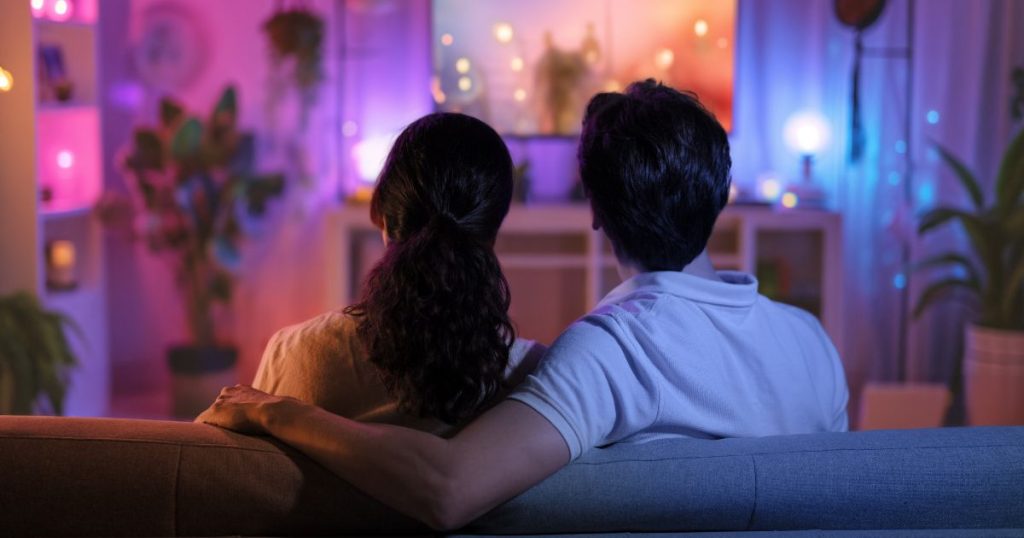 Een man en een vrouw zitten 's avonds op de zetel voor de televisie. Er branden verschillende sfeerlichtjes in de ruimte.