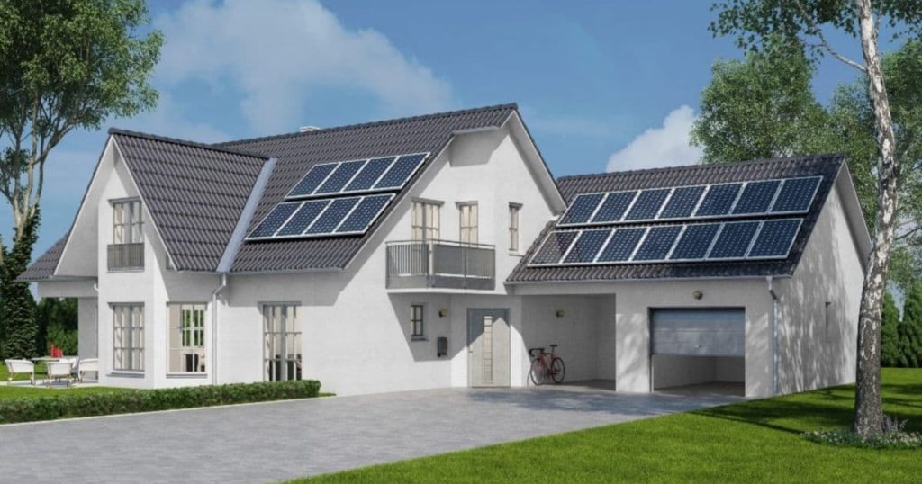een groot wit huis met grijze daken waarop zonnepanelen liggen. Er is een grote oprijlaan en een voortuin met groen gras te zien. Naast het huis staat een boom