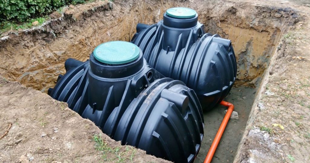 Twee zwarte stookolietanks in kunststof in een recent gegraven put. Een rode pijpleiding verbindt de stookolietanks met een centrale verwarming.