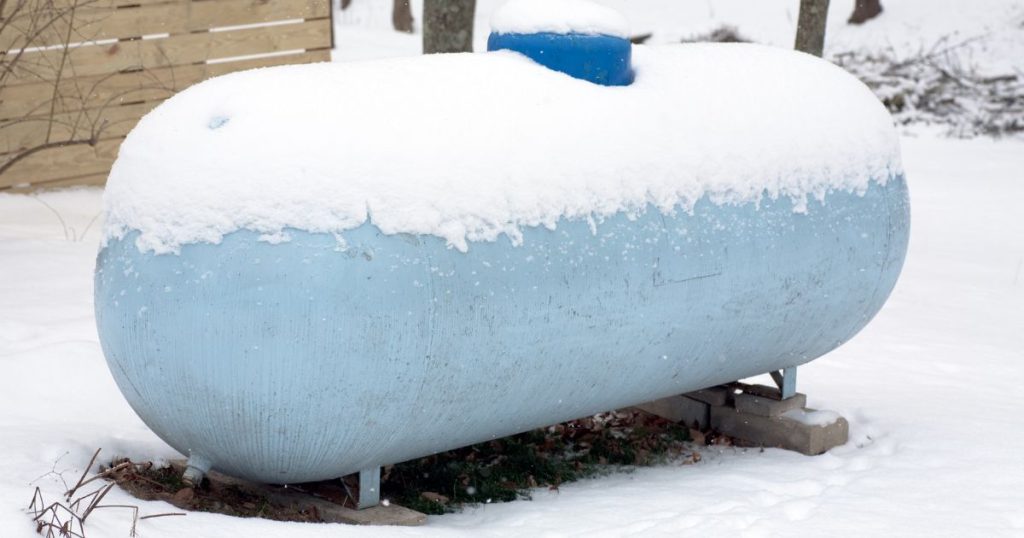 Een lichtblauwe mazouttank of stookolietank bedekt met een laag sneeuw in een ondergesneeuwde tuin.