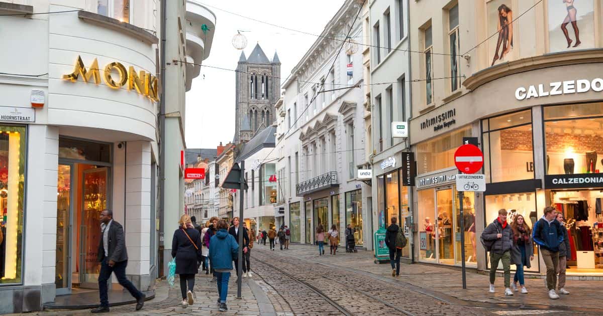 Zicht op een winkelstraat in Gent, met aan beide kanten van de weg wandelaars. In het midden van de straat ligt een trambedding.
