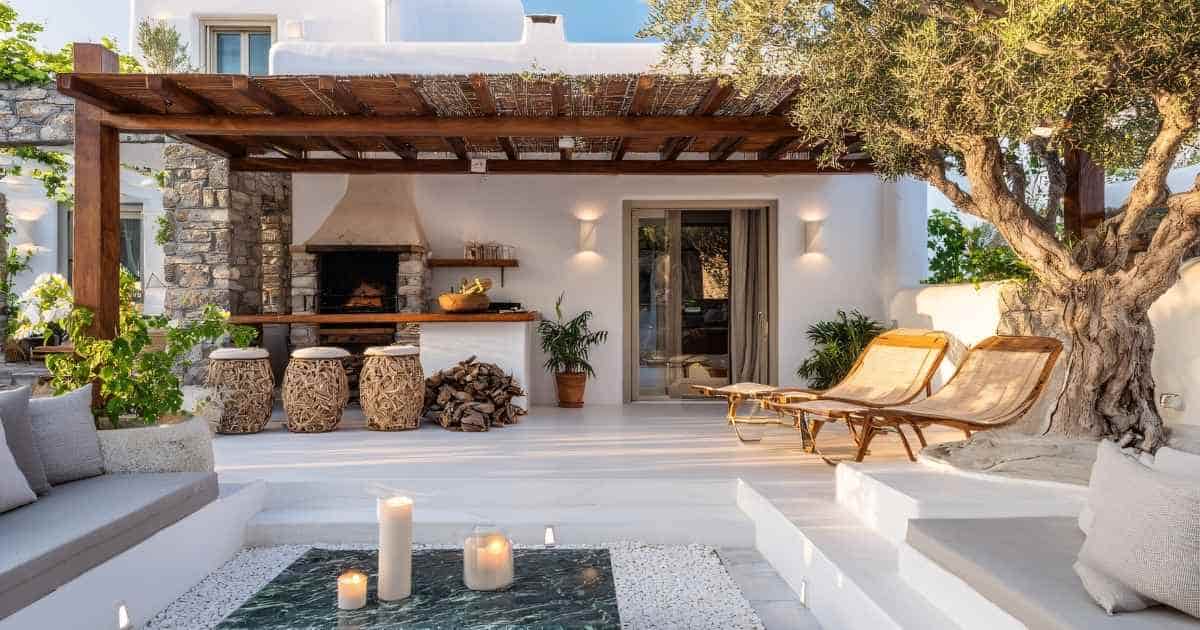 Een luxe terras uit witte natuusteen, voorzien van een ingebouwde lounge met conversatieput, overkapping, oven, comfortabele ligstoelen, bar en moderne barkrukken.