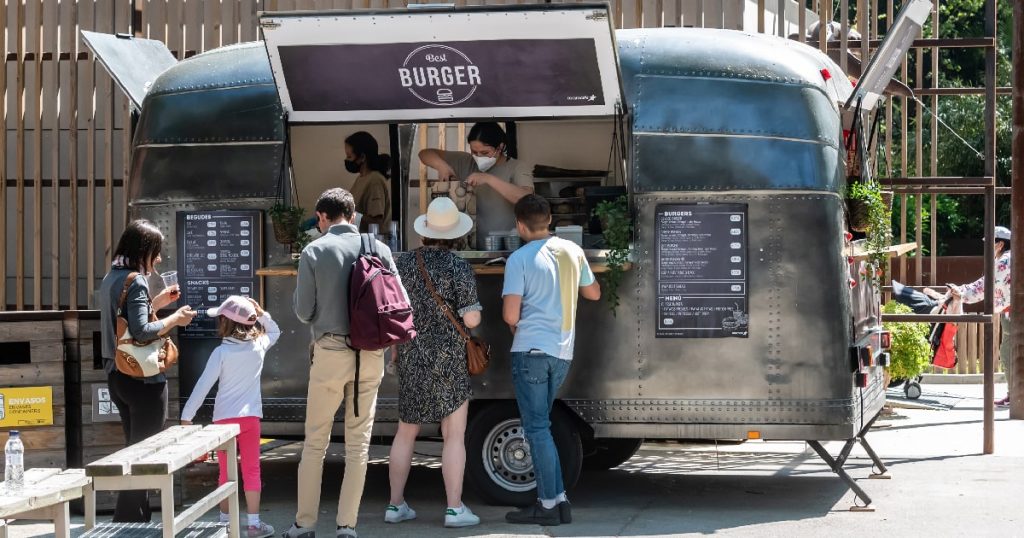 Een grijze foodtruck verkoopt burgers aan enkele toeristen.