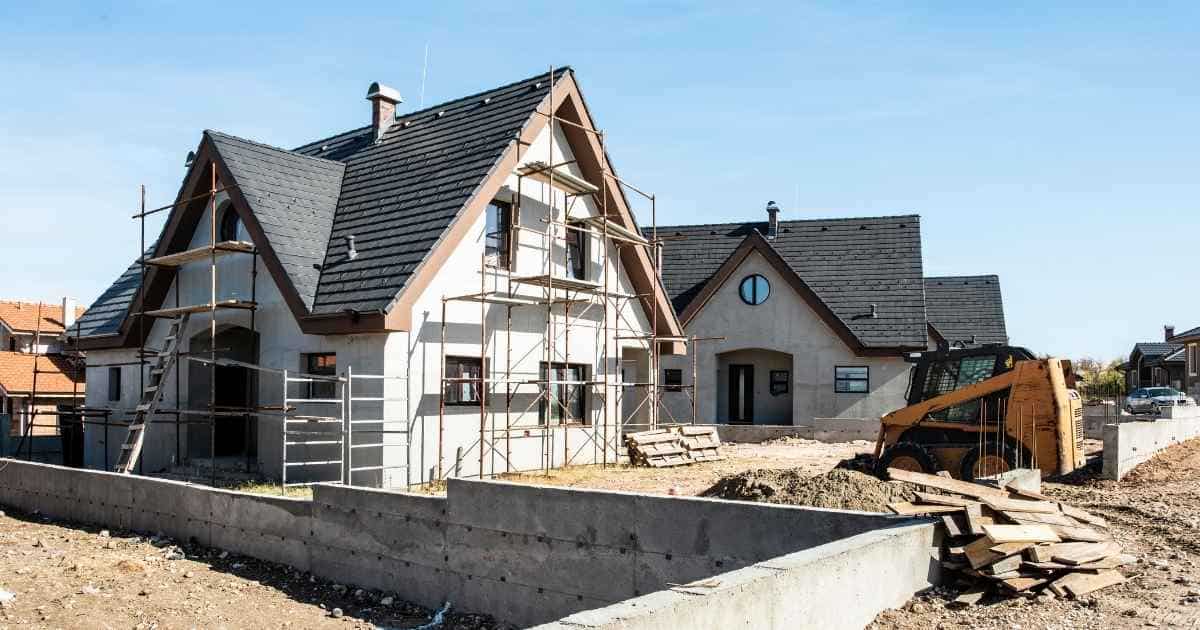 Een huis dat verbouwd wordt. Rond het huis staan stellingen. Het huis heeft een witte gevel en een zwart hellend dak met dakkapel.