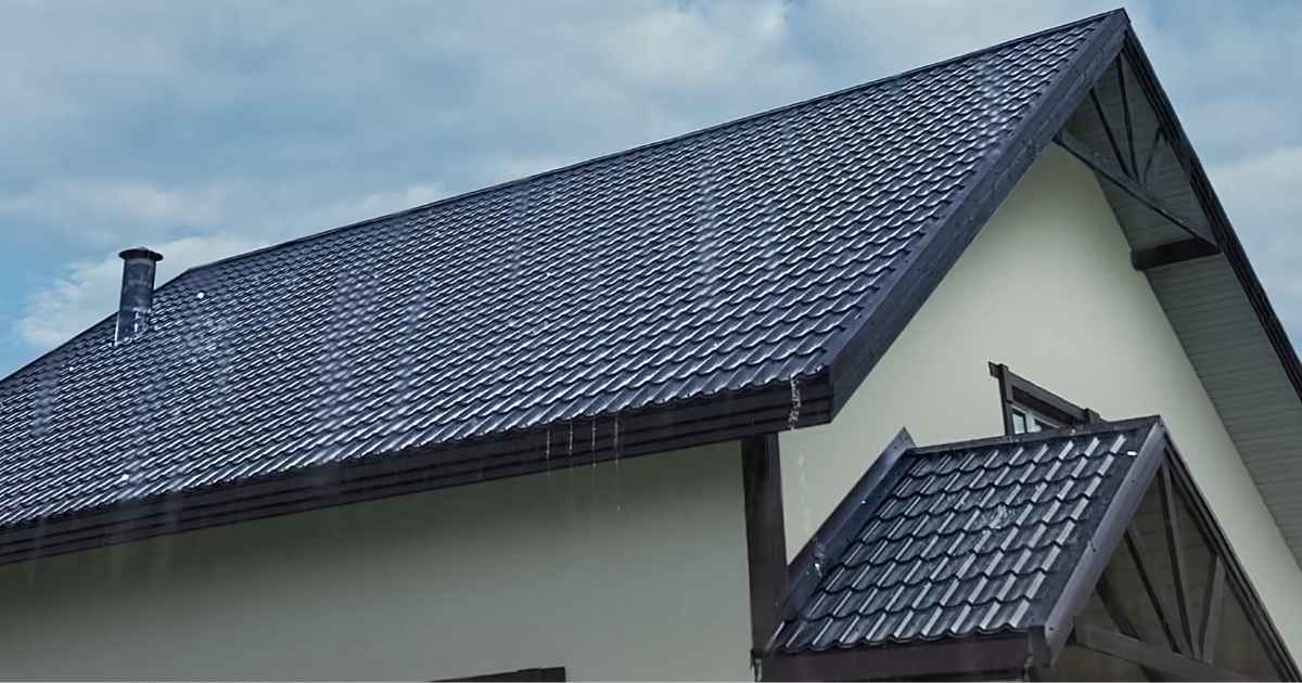 Een woning met witte gevel en een dak met donkere, grijsblauwe sandwichpanelen met dakpanprofiel.