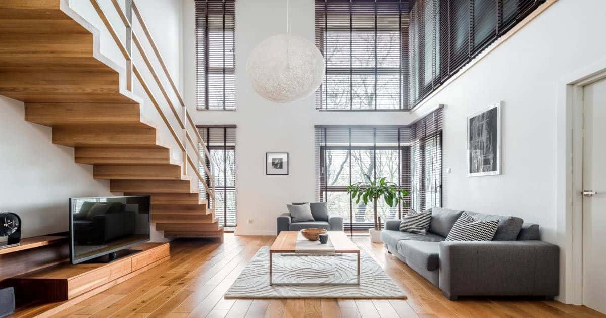 Houten trap in een moderne woonkamer: vloer is parket, een grijze zetel aanwezig, een flatscreen enzovoort.