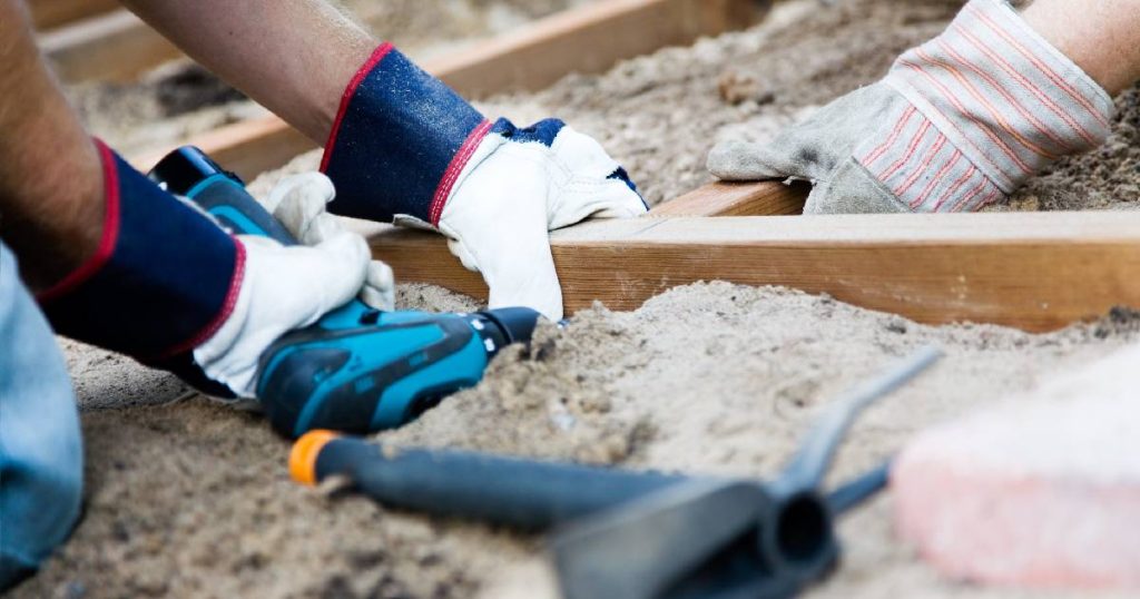 Twee mannen maken samen zelf een veranda. Ze duiden het begin van de fundering aan met van houten balken.