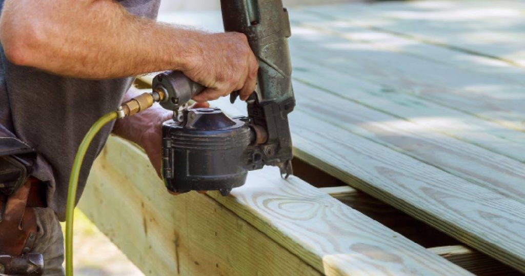 Een man is zelf een houten veranda aan het maken. Hij boort houten planken op de dakconstructie.