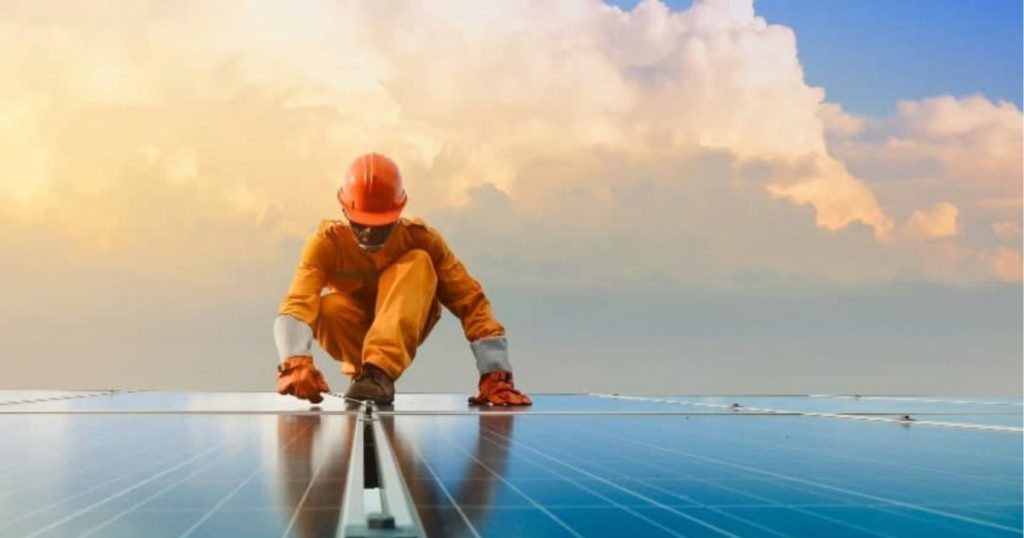 Een man in oranje werkkledij die zonnepanelen in West-Vlaanderen plaatst.