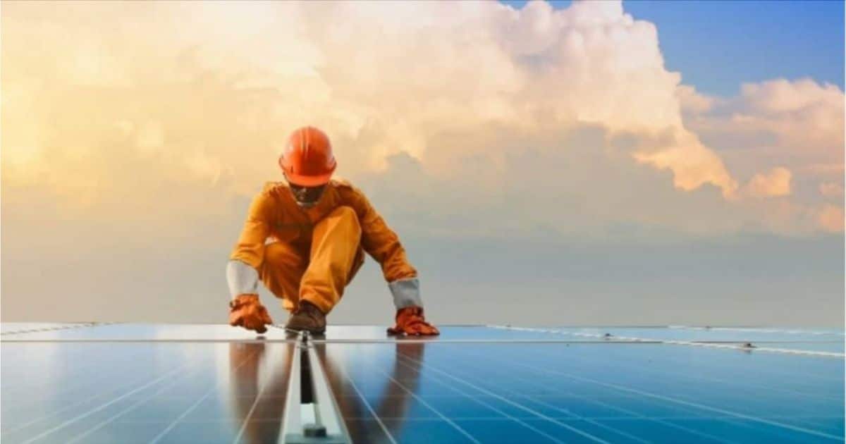 Een man die zonnepanelen in West-Vlaanderen plaatst op een plat dak. De man draagt oranje werkkledij en een helm.