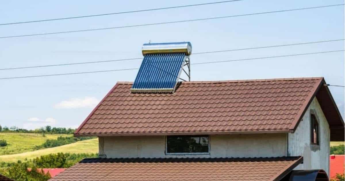 Een woning met vaalwitte gevel en een bruin hellend pannendak. Op de nok van het dak staat een grote blauwe zonnecollector voor een zonneboiler.
