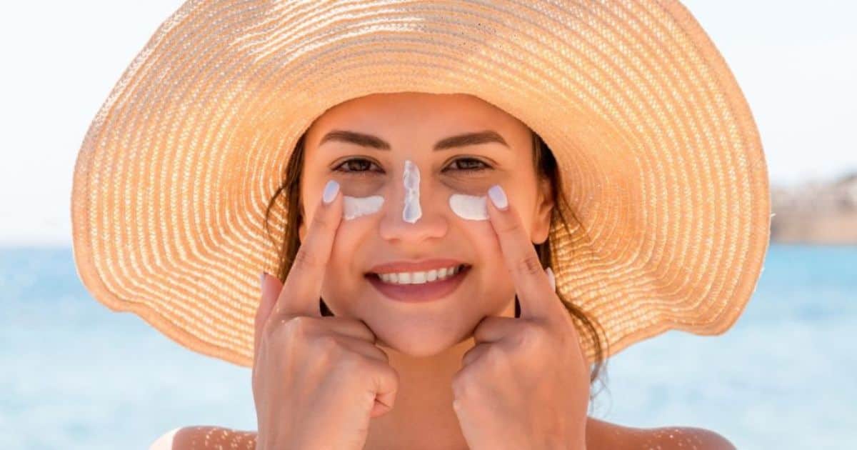 Een dame met zonnehoed brengt zonnecrème aan op haar neus en wangen.
