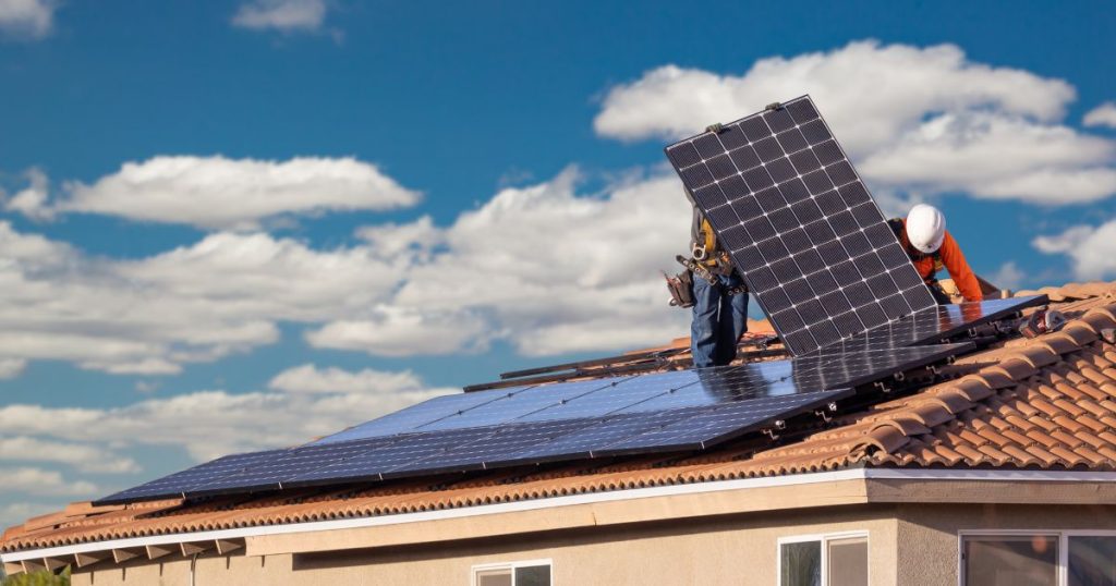 Twee installateurs plaatsen zonnepanelen op een oranje pannendak.