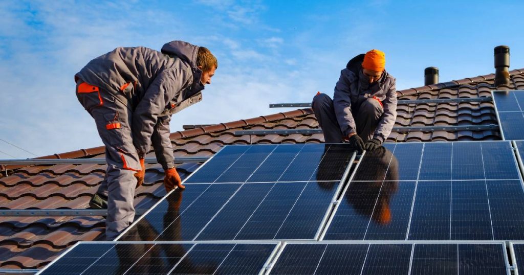 Twee zonnepaneelinstallateurs installeren zonnepanelen verticaal op een dak met lichte schaduw.