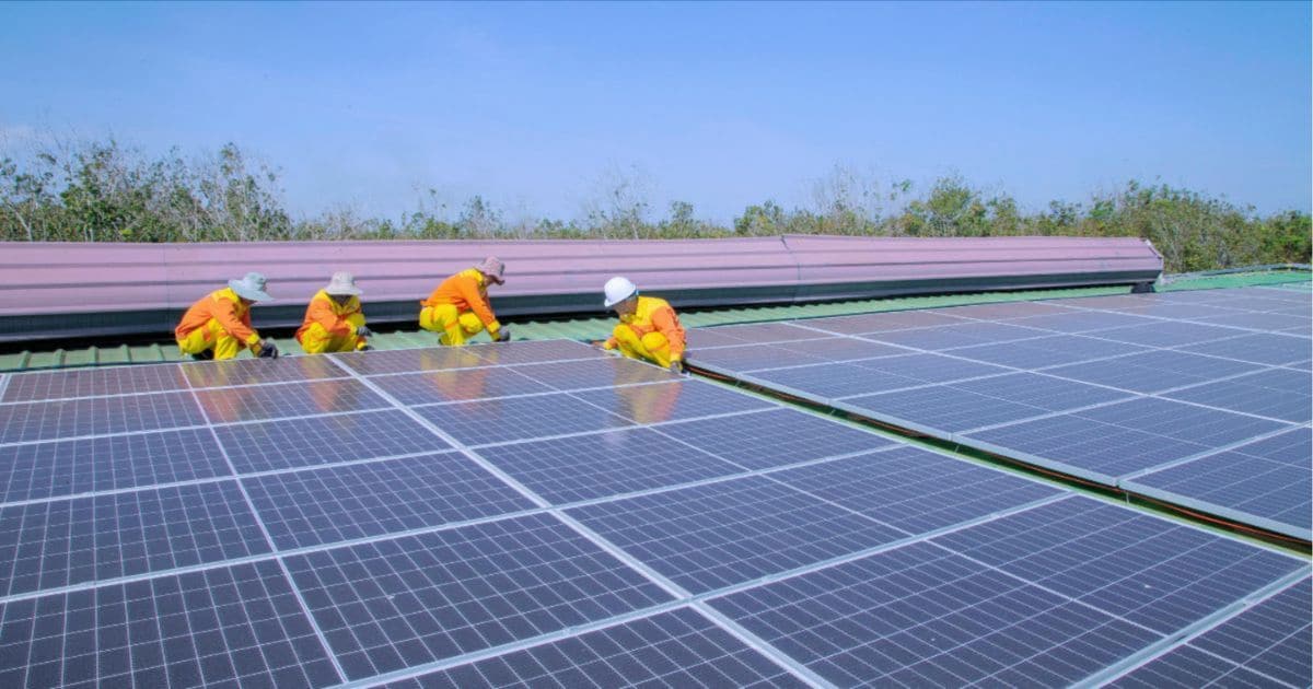 Vier mannen in Ieper installeren zonnepanelen op een dak. De zonnepanelen worden geïnstalleerd op een plat dak.
