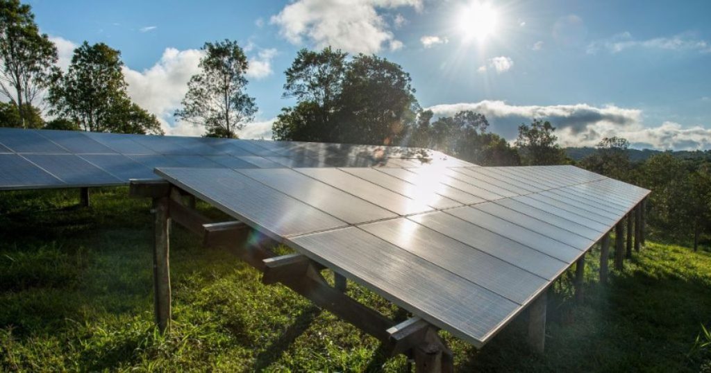 Een zonnepanelen installatie op een open stuk weiland  in een bosrijke omgeving.