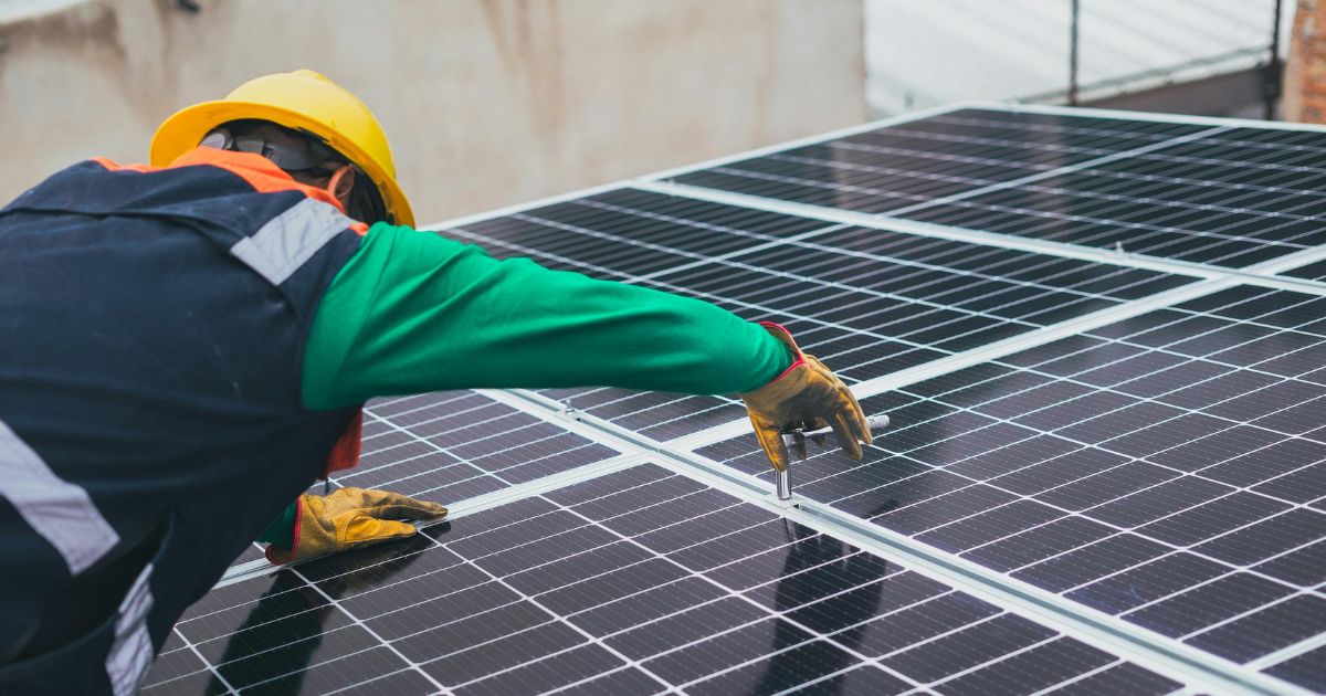 Een installateur schroeft de zwarte panelen vast op een lichthellend dak.