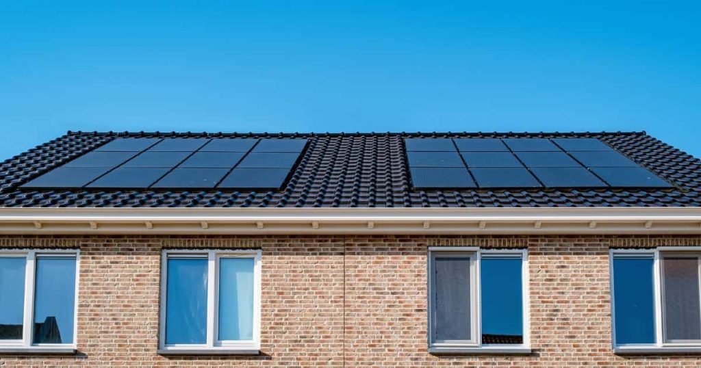 Twee halfopen woningen met identieke gevel, ramen, dak én zonnepanelen. De lucht is hemelsblauw. Dat wil zeggen dat de zon fel schijnt en dat je panelen veel zonne-energiei opwekken.