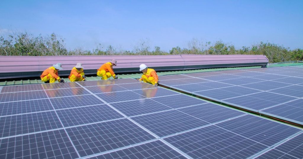 Vier mannen installeren zonnepanelen op een dak. Ze dragen werkkleding en helmen voor bescherming.