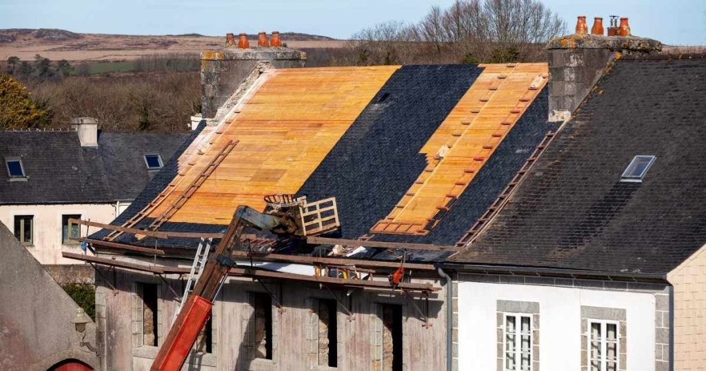 Overzicht van een woning waarvan het dak grondig gerenoveerd wordt. Er liggen houten latten op het dak. Er staat een bouwkraan tegen de woning.