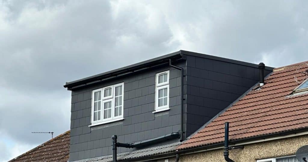 Een zwarte uitbouw op een rood pannendak. De uitbouw beschikt over kleine ramen met witte kozijnen en kruishouten.