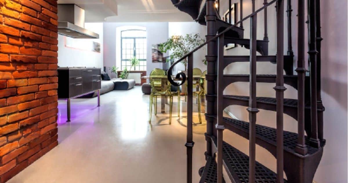 Een zwarte, metalen wenteltrap in een modern interieur naast een bakstenen muur.