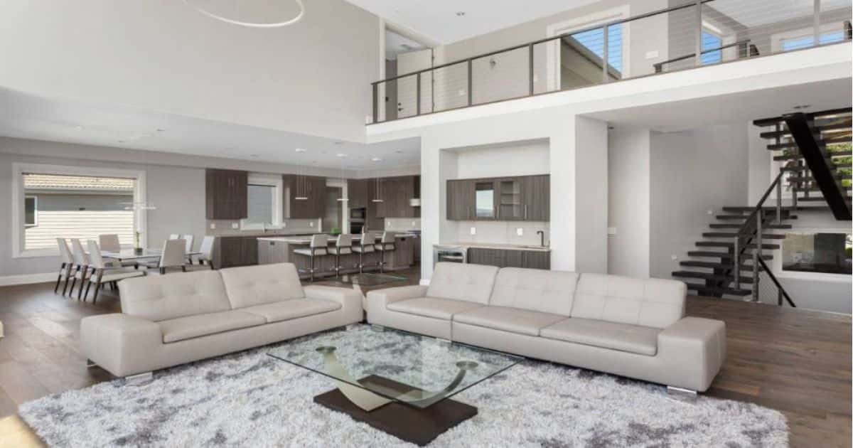 Een zwarte open trap in een modern interieur met twee grijze zetels en een glazen koffie tafel.