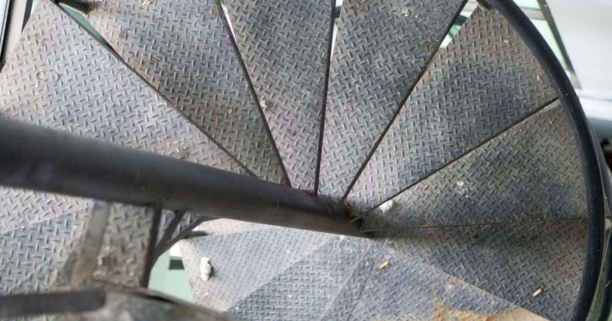 Detail van een metalen wenteltrap die beneden uitkomt op een groenachtige vloer.