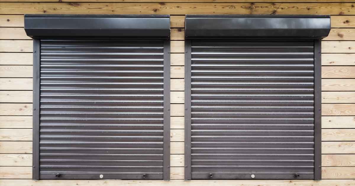 Twee ramen met zwarte rolluiken in pvc in een houten gevel.