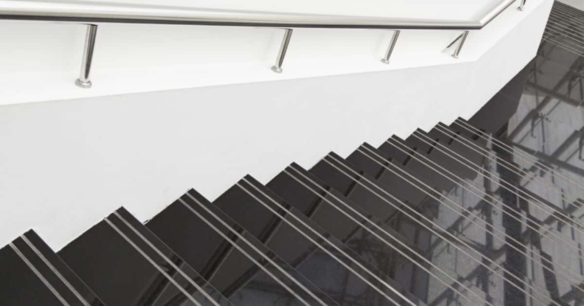 Een zwarte trap met zwarte marmeren treden en een zilveren metalen trapleuning, in combinatie met witte muren