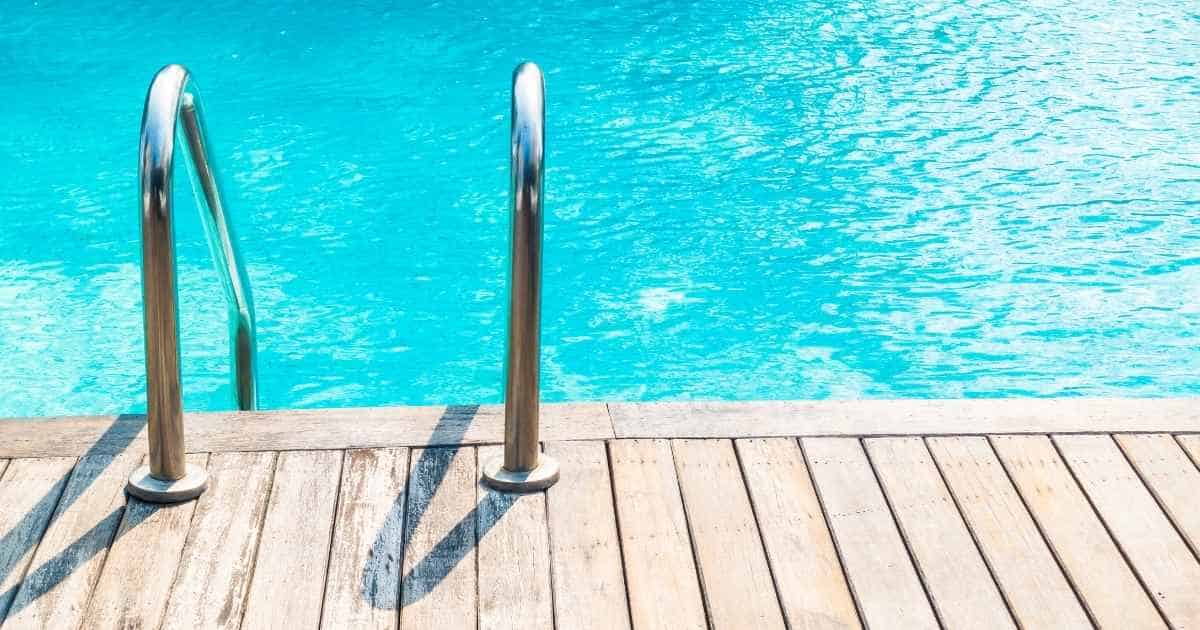 Een zwembad met helder blauw water en een roestvrijstalen trap. De rand van het zwembad werd afgewerkt met hout.